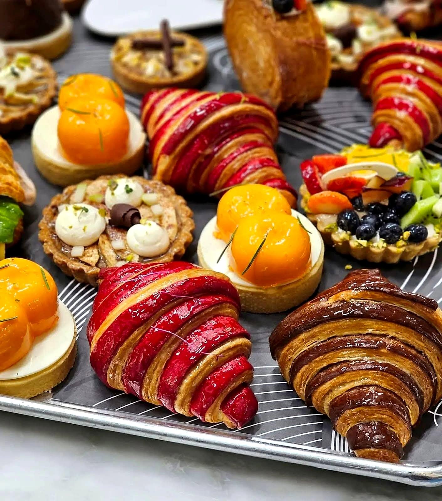 A tray of bicolour croissants, mango tarts and fruit tarts ready for service